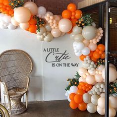 an orange and white balloon arch is on the wall next to a wicker chair