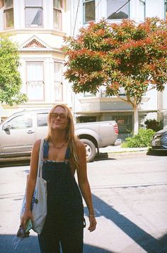 a woman is walking down the street in front of some parked cars and buildings with her eyes closed