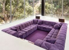 a large purple couch sitting in front of a tall window with lots of windows on each side