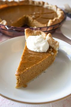 a slice of pumpkin pie on a plate with a fork and bowl in the background