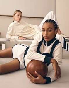 two women in white and black outfits, one holding a football while the other is laying down