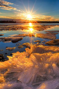 the sun is setting over some ice floes on the water's edge, and it appears to be melting