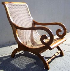 a wooden chair sitting on top of a sidewalk next to a white wall and cement floor