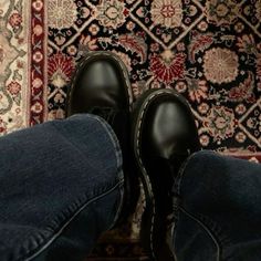 a pair of black shoes sitting on top of a rug next to a person's legs