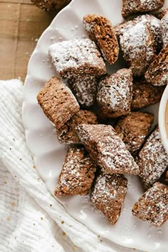 a white plate topped with brownies next to a cup of coffee and powdered sugar