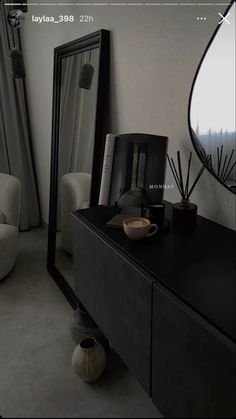 there is a black dresser with a mirror on it next to a chair and vase