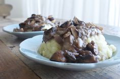 two plates filled with mashed potatoes covered in gravy on top of a wooden table