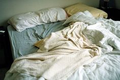 an unmade bed with white sheets and pillows