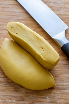 two pieces of yellow food sitting on top of a cutting board next to a knife