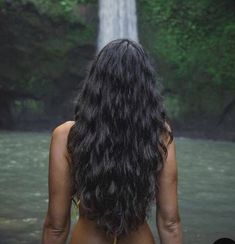 a woman standing in front of a waterfall with her back turned to the camera,