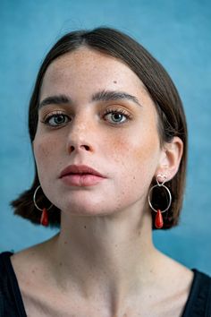 a woman with freckles on her face looking at the camera and wearing earrings