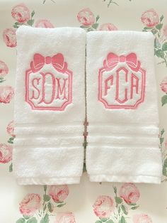 two white towels with pink bows and monogrammed letters on them are sitting next to each other