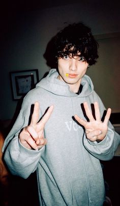 a young man making the peace sign with his hands in front of him and wearing a grey hoodie