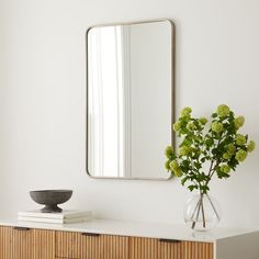 a vase with flowers on top of a dresser next to a mirror and bookcase