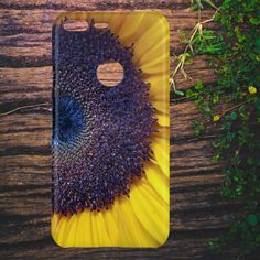 a phone case with a sunflower in the center on a wooden table next to green plants