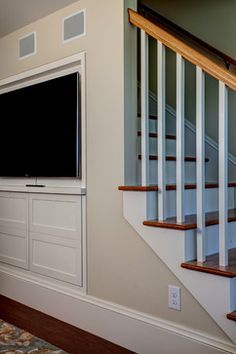 a tv mounted on the wall in a living room next to a stair case and window