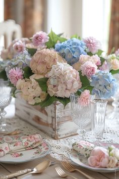 a table set with plates, silverware and pink and blue flowers in a vase