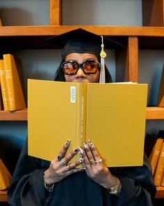 a woman in graduation gown holding up a yellow book