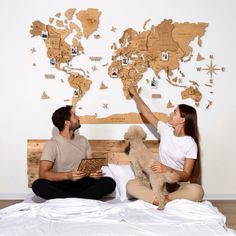 a man and woman sitting on a bed with a dog in front of a world map