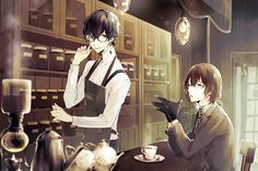 two people sitting at a table in front of stacks of books and cups, one holding a book