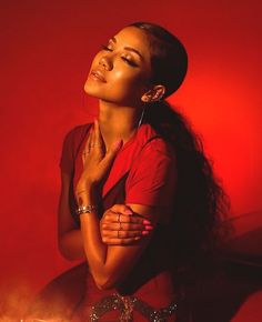 a woman standing in front of a red wall with her hands on her chest and eyes closed