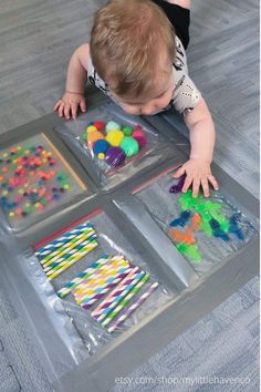 a baby crawling on the floor in front of four plastic trays filled with different colored candies