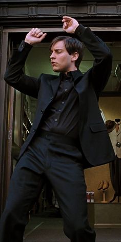 a man in a black suit is posing for the camera with his hands on his head