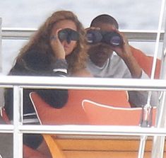 two people sitting on a boat looking through binoculars at the ocean while another person sits in an orange chair