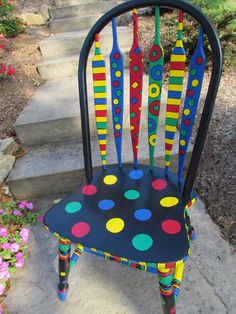 a colorful painted chair sitting on the side of a sidewalk next to flowers and steps