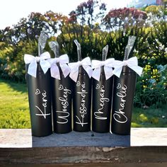 four black wine bottles with white bows and names on them sitting on a wooden table