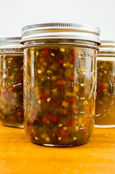 three jars filled with pickled peppers on top of a wooden table and text overlay that reads, sweet & spicy pepper jelly