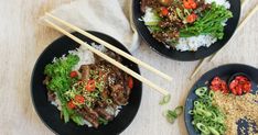 three black plates topped with meat and veggies next to chopsticks on a table