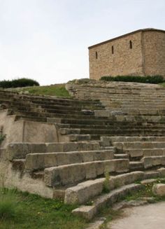 an old stone building sitting on top of a hill next to grass and rocks with steps leading up to it