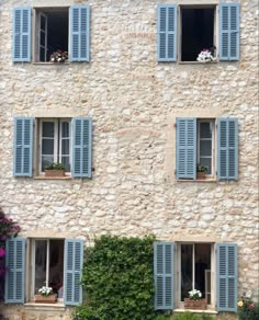 an old building with blue shutters and flowers in the window boxes on either side