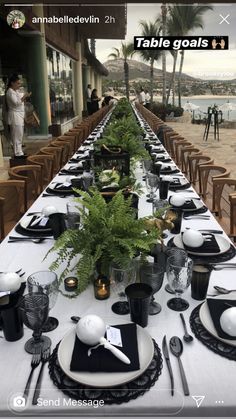 a long table set with black and white plates, silverware and greenery on it