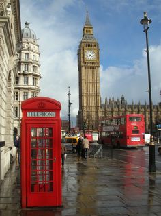 a red phone booth sitting on the side of a road next to a tall clock tower