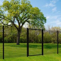 a black metal fence in the middle of a grassy field next to a large tree