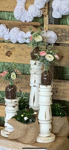 three white vases with flowers in them sitting on top of burlocked fabric