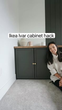 a woman sitting on the floor in front of some cupboards and smiling at the camera