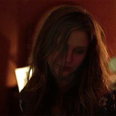 a woman with long hair is looking down at her cell phone while standing in a dark room