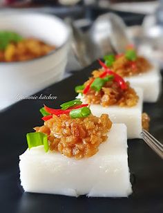 three pieces of food on a black plate with silverware and bowls in the background