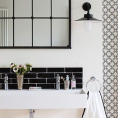 a white sink sitting under a mirror next to a black and white tiled wallpaper