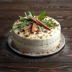 a carrot cake on a wooden table with cinnamons and sprigs around it