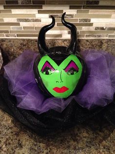 a green mask with horns and purple tulle around it's face on a counter top