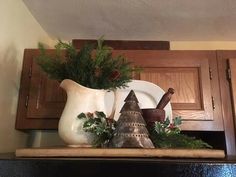 a white pitcher filled with greenery sitting on top of a wooden shelf next to a plate