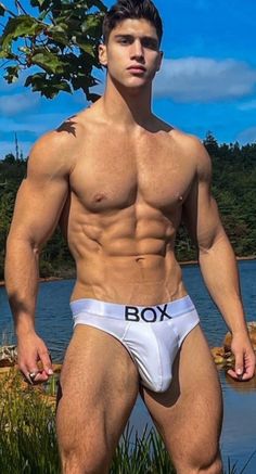 a shirtless man standing in front of a body of water with his hands on his hips