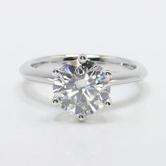 a white gold engagement ring with a round brilliant cut diamond in the center, on a plain surface