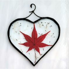 a glass heart with a red leaf hanging from it's side on a white surface