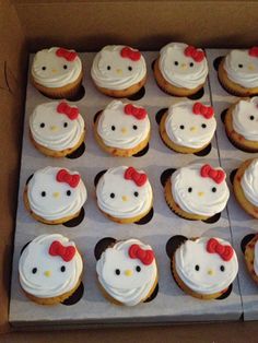 cupcakes with white frosting and red bows are arranged in a cardboard box