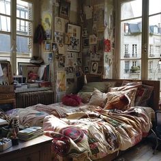 an unmade bed sitting in a bedroom next to two windows with pictures on the wall